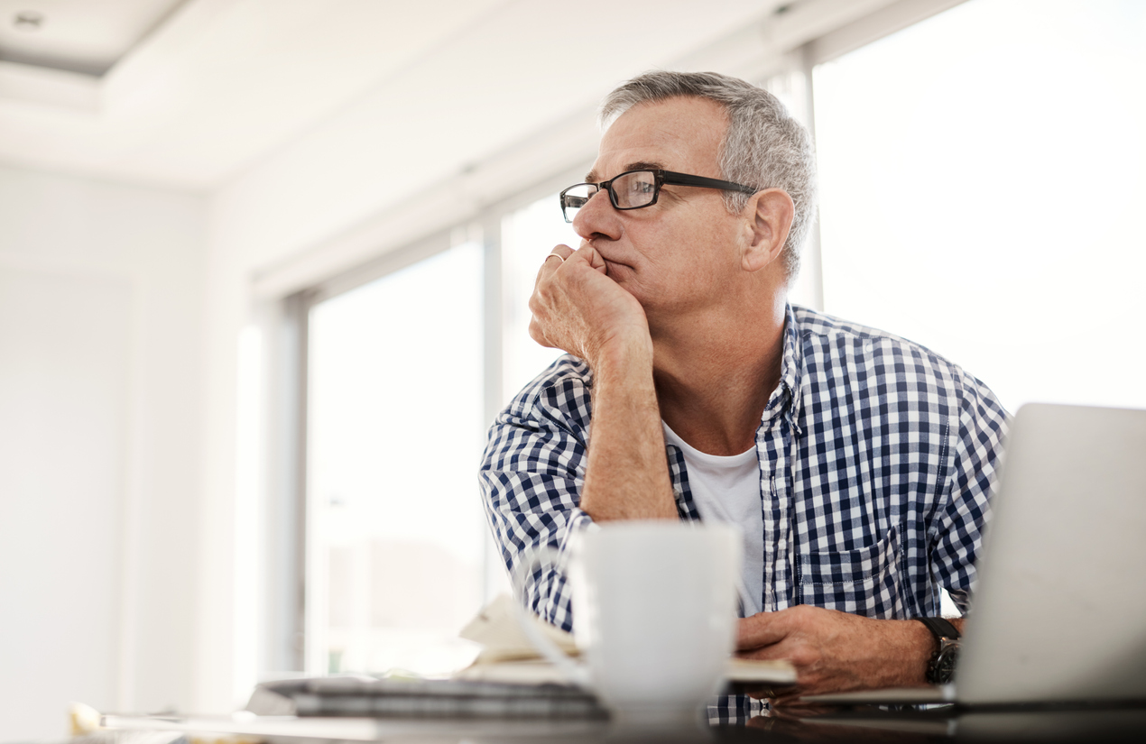 Shot of a mature man looking thoughtful while working on a laptop at home