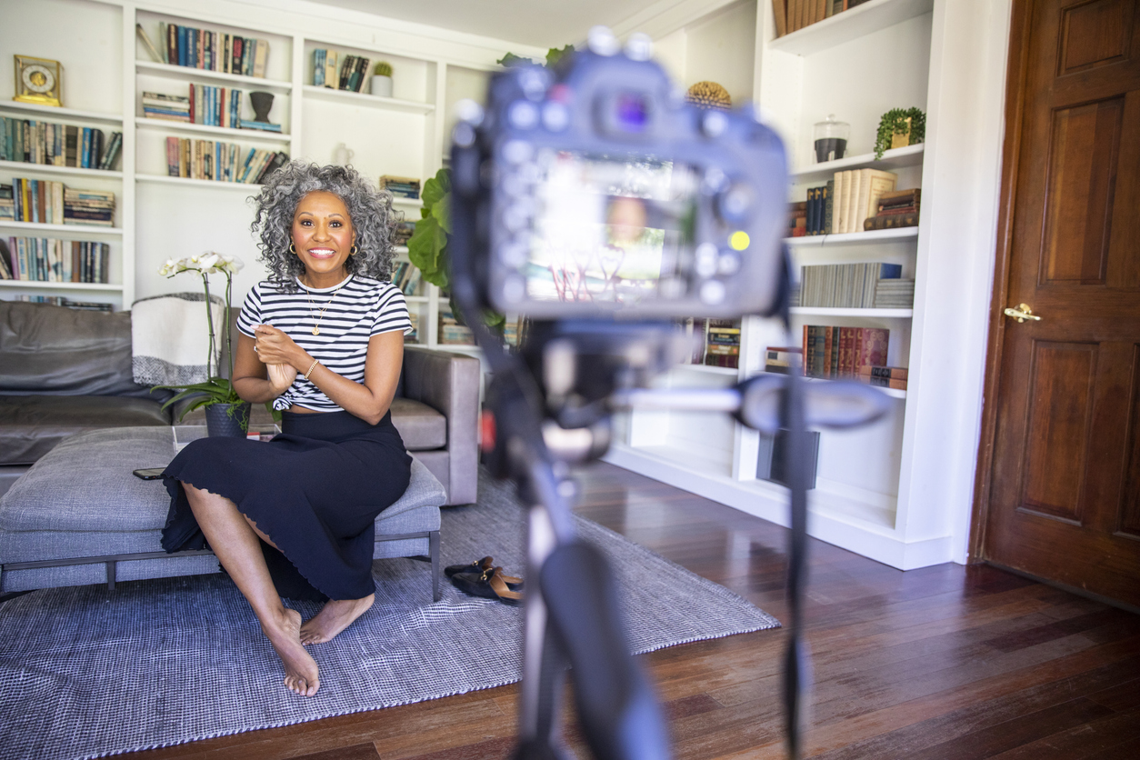 A beautiful black woman with white curly hair sets up her camera and tripod to record a vlog for her blog
