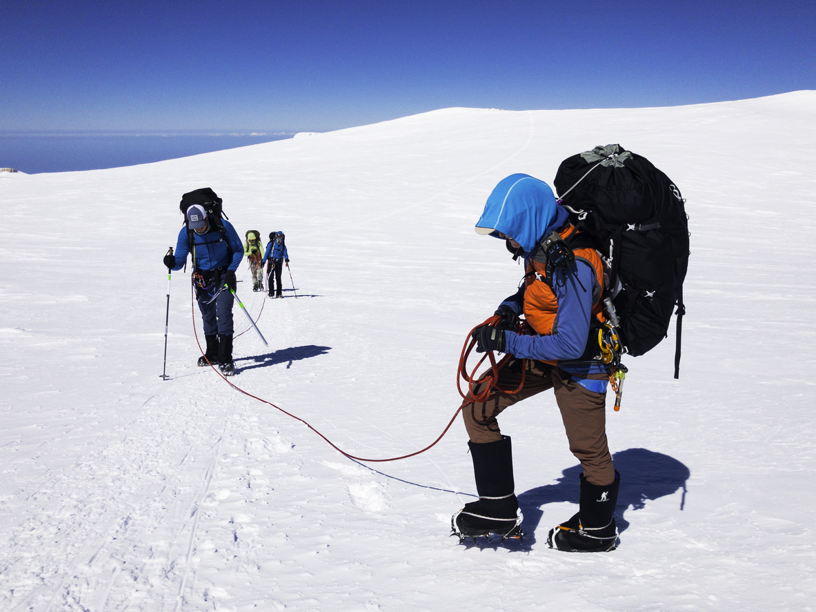 Adult male backpacker hiking in front of non-urban scene / landscape - scenery / mountain peak / mountain range / nature who is outdoors wearing backpack / climbing who is conquering adversity who is exploration and using rope / hiking pole / sky / mountain
