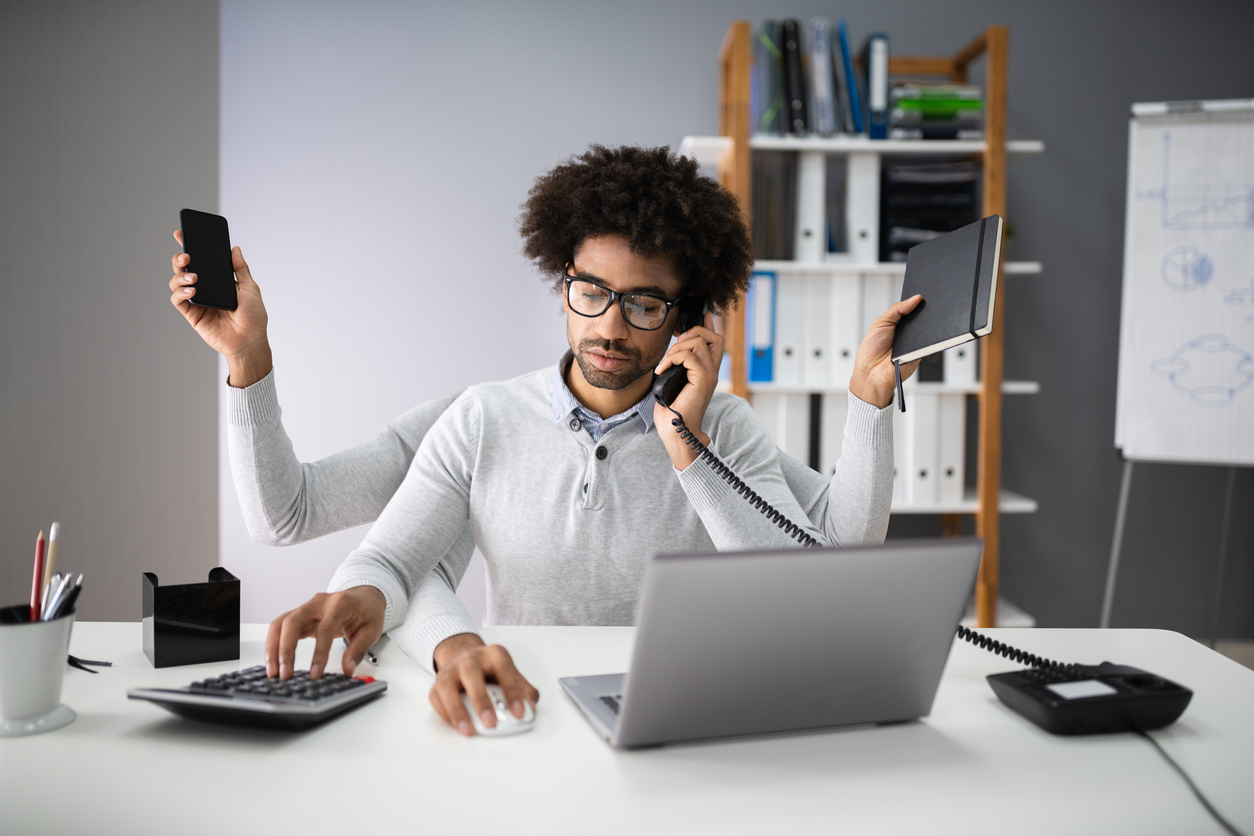 Smiling Young Businessman Doing Multitasking Work At Workplace