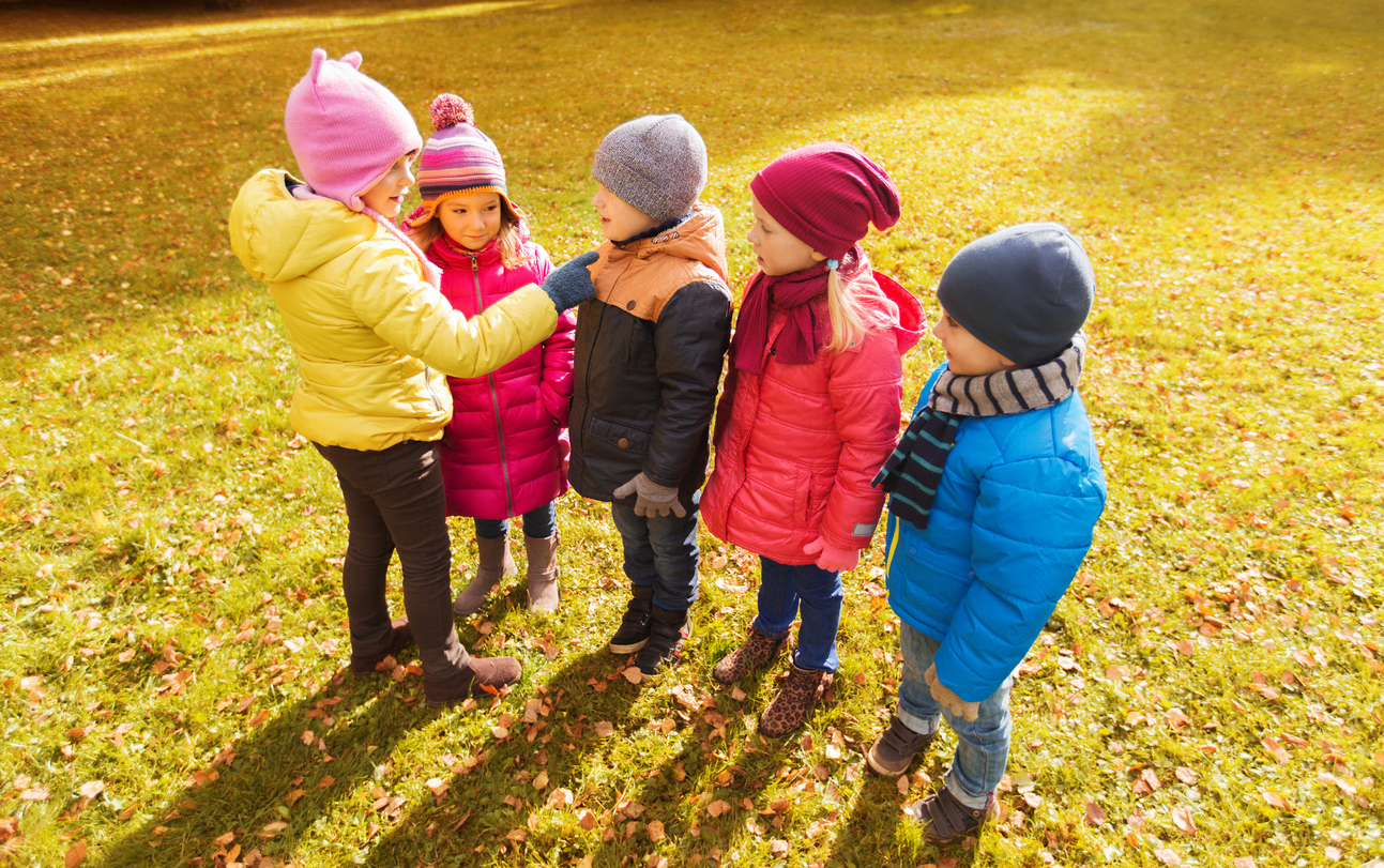 childhood, leisure, friendship and people concept - group of happy kids in autumn park counting and choosing game leader