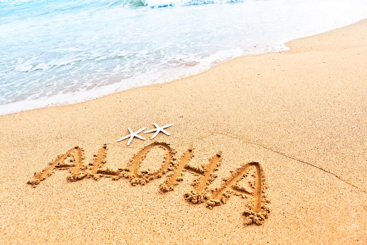 The Hawaiian greeting of hello "aloha" written on the sandy beach of Hawaii, greeting vacationers to the islands.