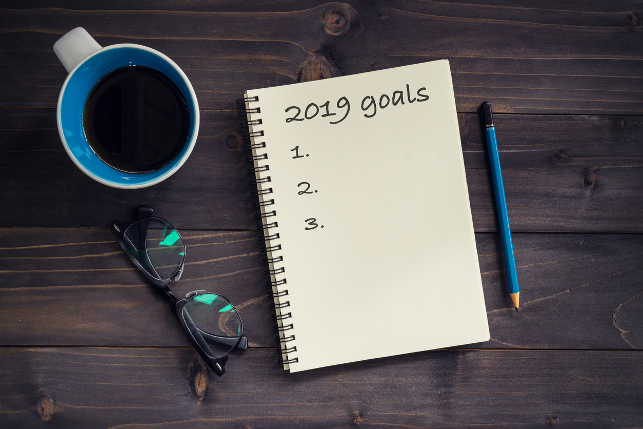 Notebook with 2019 goals massage, pencil, glasses and cup of coffee on wood background.